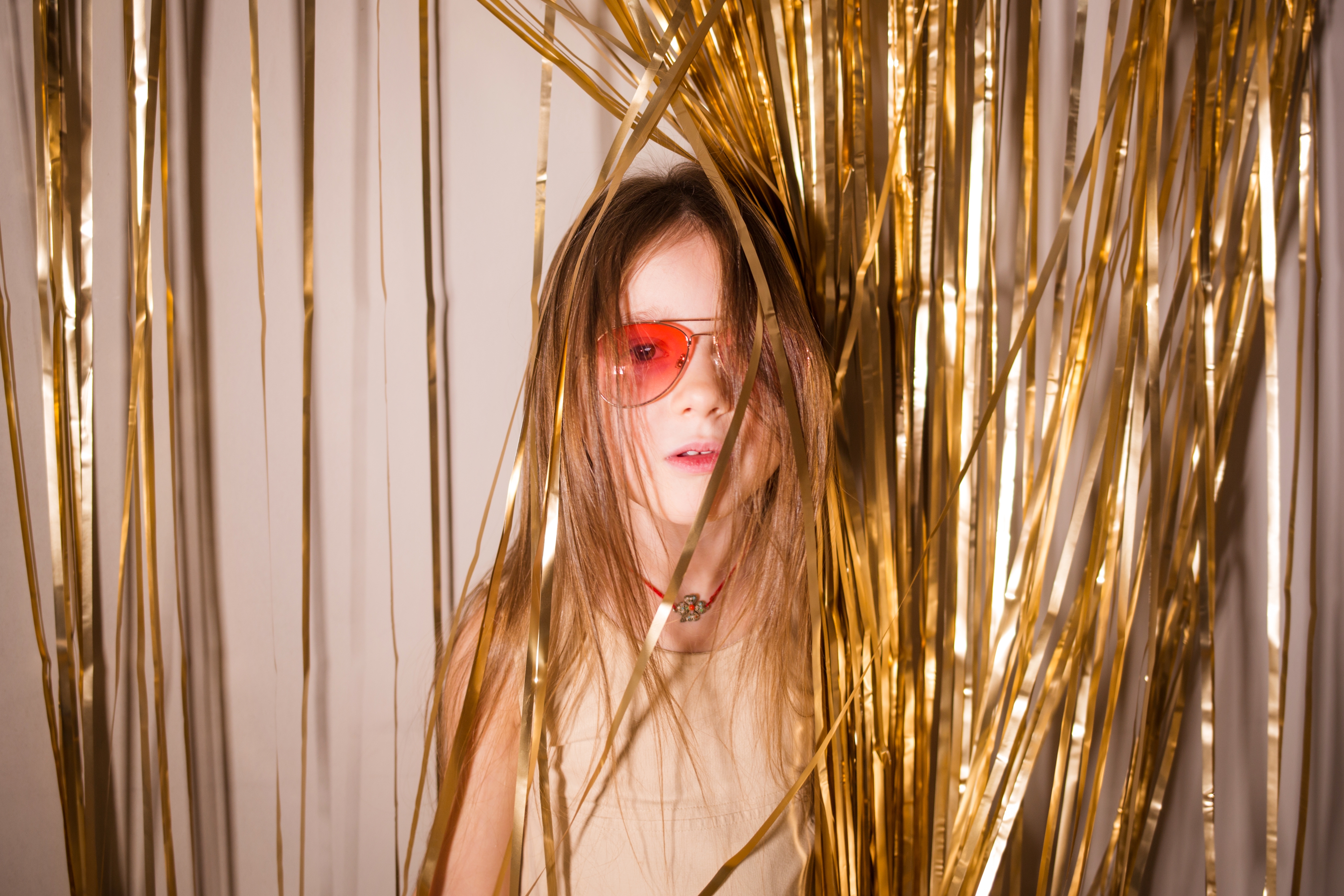 stylish model baby child girl in pink glasses on background of golden tinsel. concept of holiday,